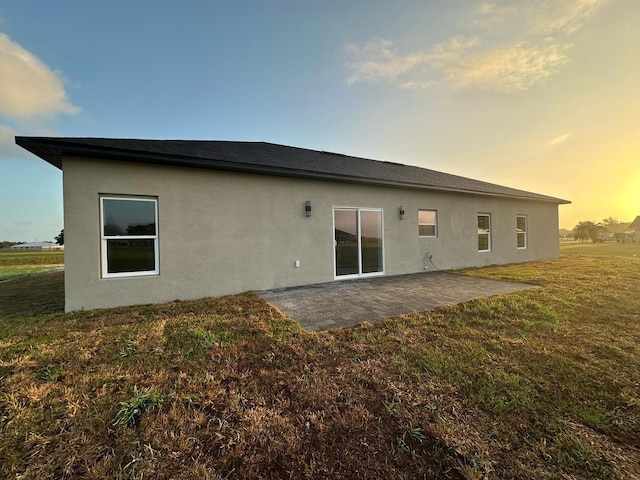 back of house at dusk featuring a patio area, stucco siding, and a lawn