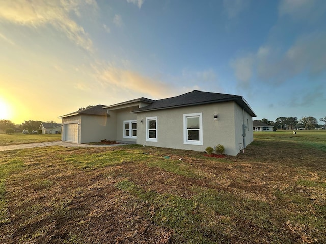 rear view of property with a lawn, driveway, stucco siding, and an attached garage