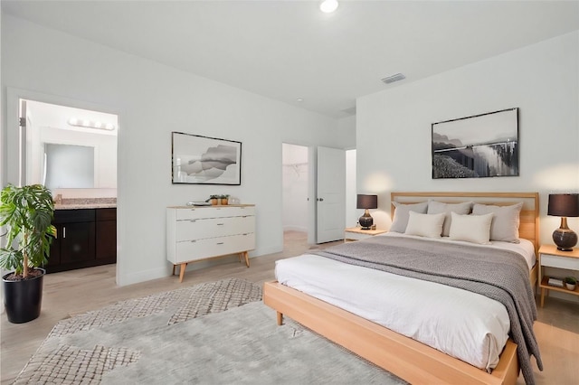 bedroom featuring a walk in closet, baseboards, light wood-style flooring, and ensuite bathroom