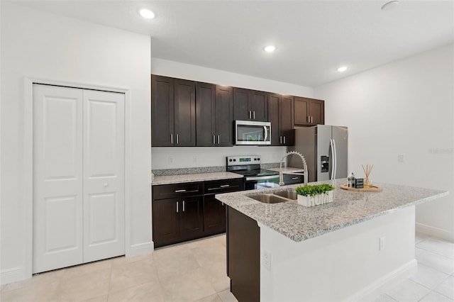 kitchen with appliances with stainless steel finishes, a kitchen island with sink, a sink, light stone countertops, and baseboards