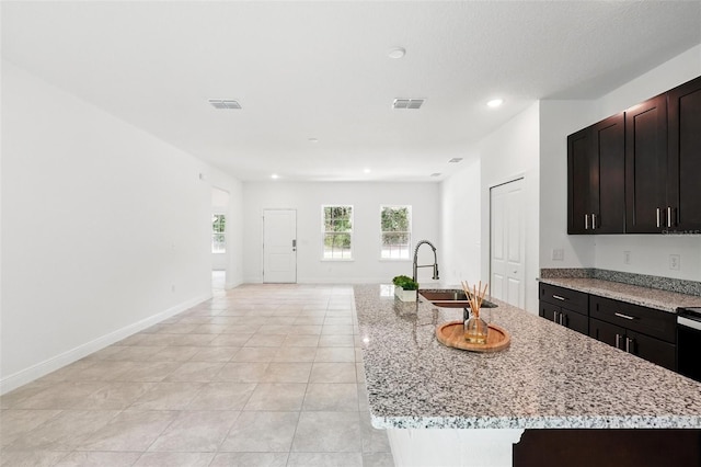 kitchen with a sink, an island with sink, recessed lighting, light tile patterned floors, and light stone counters