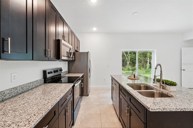 kitchen featuring stainless steel appliances, a sink, a kitchen island with sink, recessed lighting, and light stone counters