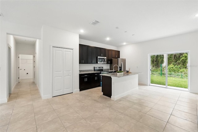 kitchen with stainless steel appliances, an island with sink, light tile patterned floors, recessed lighting, and light stone counters