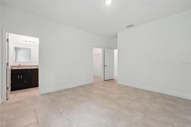unfurnished bedroom with a walk in closet, ensuite bath, baseboards, and a closet