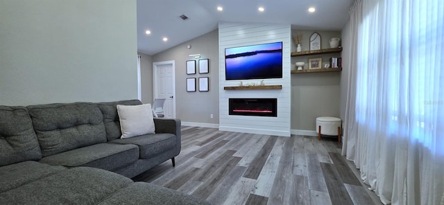 living area with vaulted ceiling, visible vents, baseboards, wood finished floors, and a large fireplace