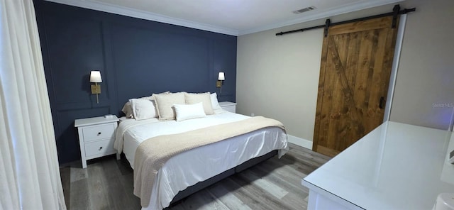 bedroom featuring a barn door, baseboards, visible vents, wood finished floors, and ornamental molding