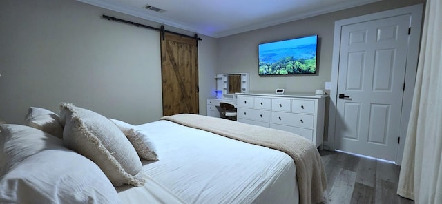 bedroom featuring wood finished floors, visible vents, a barn door, and crown molding