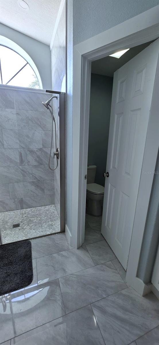 full bathroom with marble finish floor, a tile shower, a textured ceiling, and toilet
