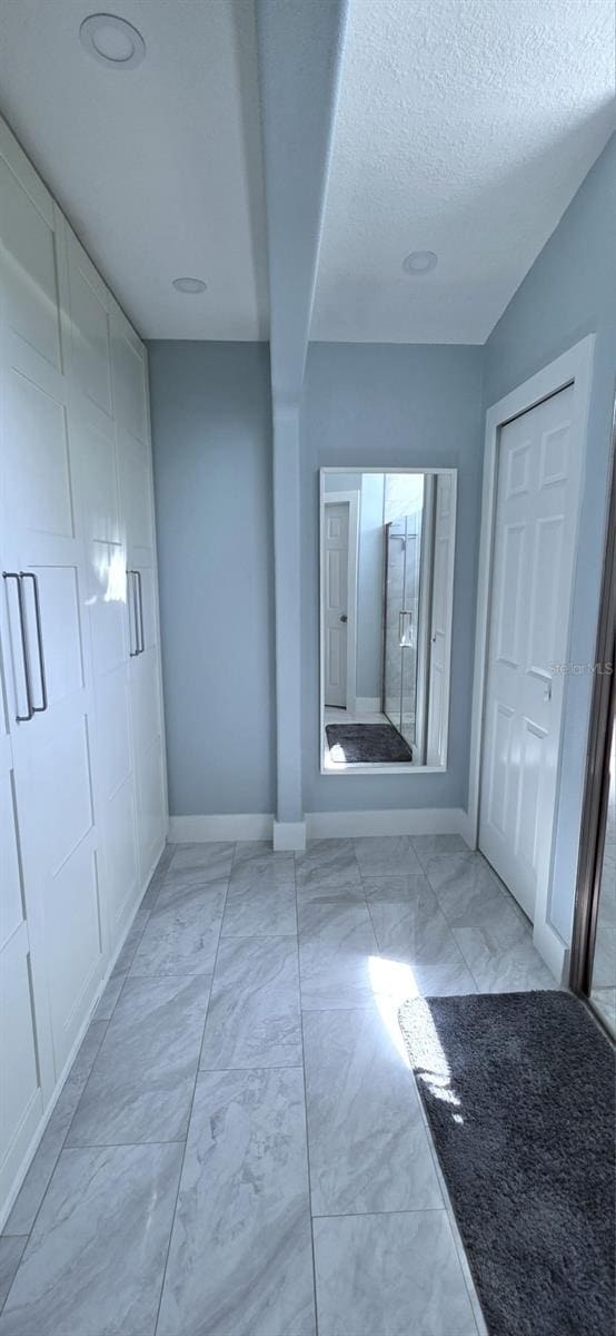hall with marble finish floor, baseboards, and a textured ceiling