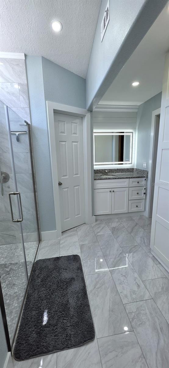 full bathroom featuring a textured ceiling, visible vents, marble finish floor, a shower stall, and vanity