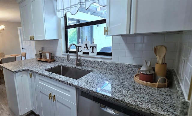 kitchen with white cabinets, a sink, a chandelier, backsplash, and light stone counters
