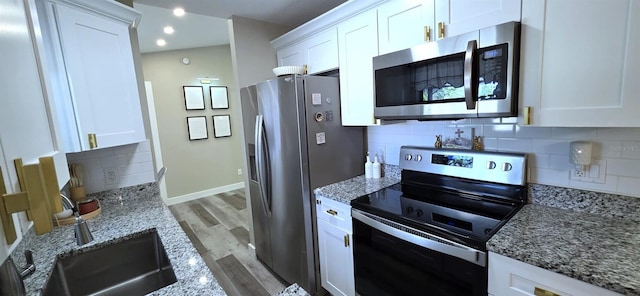kitchen featuring white cabinets, light stone countertops, light wood-style flooring, tasteful backsplash, and appliances with stainless steel finishes