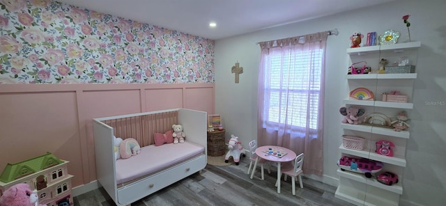 bedroom featuring wainscoting, wood finished floors, and a decorative wall