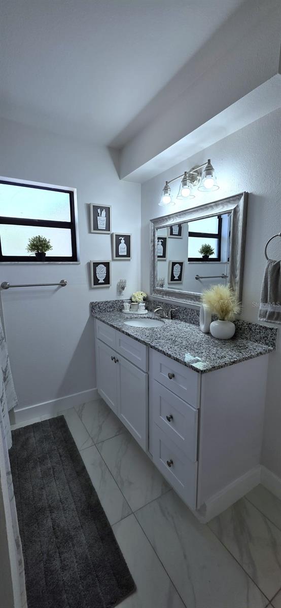 bathroom with a healthy amount of sunlight, marble finish floor, and baseboards