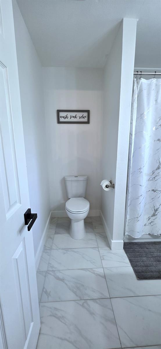 full bathroom featuring a shower with shower curtain, marble finish floor, baseboards, and toilet