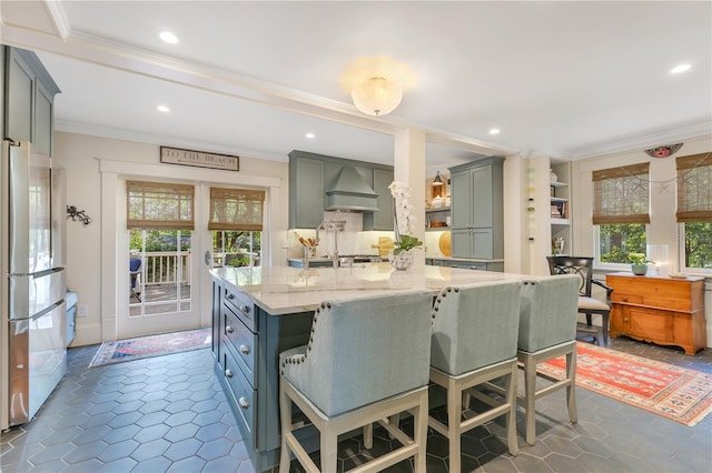kitchen with recessed lighting, crown molding, light stone counters, premium range hood, and freestanding refrigerator