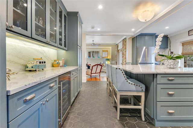 kitchen featuring beverage cooler, light stone countertops, freestanding refrigerator, a breakfast bar area, and crown molding
