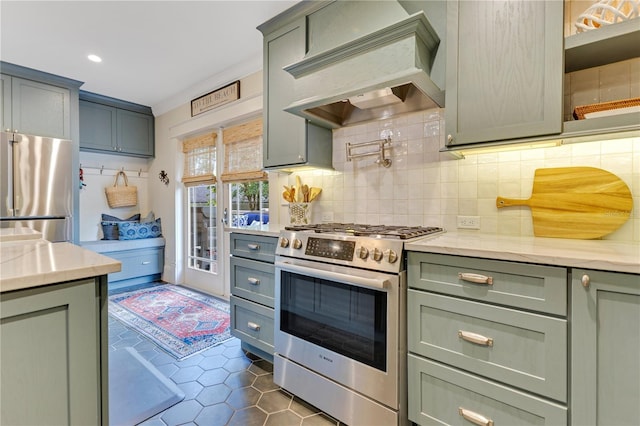 kitchen with dark tile patterned flooring, decorative backsplash, custom range hood, appliances with stainless steel finishes, and green cabinets