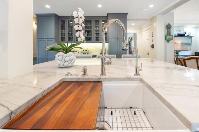kitchen with light stone counters, recessed lighting, and glass insert cabinets
