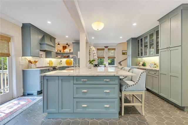 kitchen featuring custom exhaust hood, glass insert cabinets, decorative backsplash, a breakfast bar, and a sink