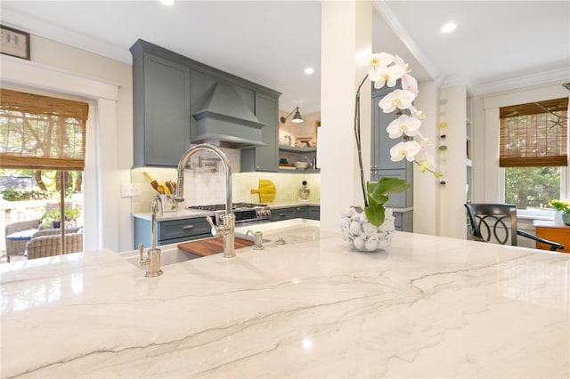 kitchen featuring gray cabinetry, premium range hood, crown molding, and light stone counters