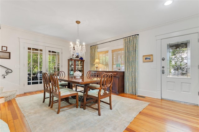 dining area with light wood-type flooring, ornamental molding, an inviting chandelier, and french doors