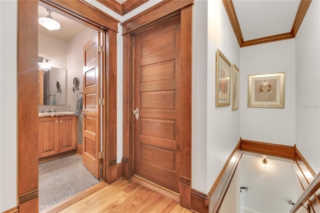 corridor featuring ornamental molding, light wood-style flooring, and a sink
