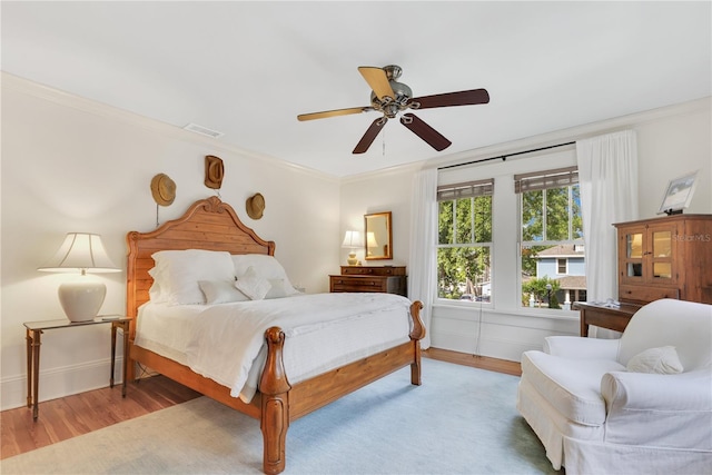 bedroom with wood finished floors, baseboards, visible vents, a ceiling fan, and crown molding