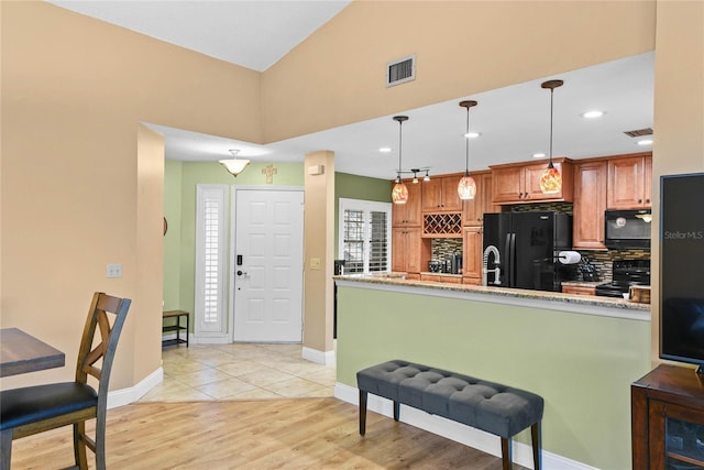 kitchen featuring pendant lighting, light stone counters, visible vents, and black appliances
