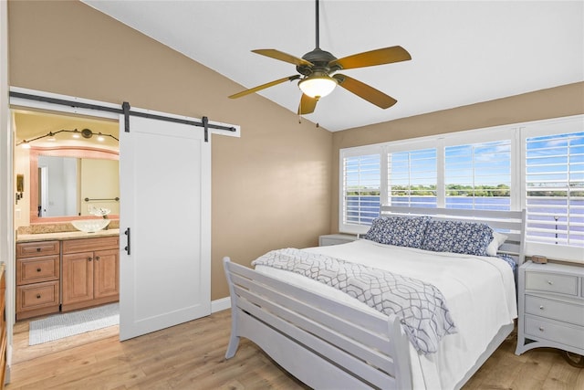 bedroom with a water view, a barn door, light wood-style flooring, and vaulted ceiling