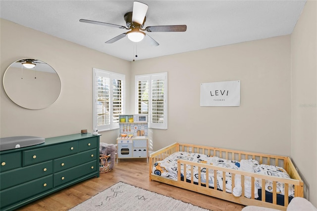bedroom featuring a nursery area, a ceiling fan, and wood finished floors