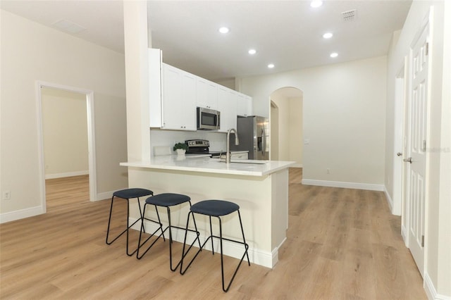 3835 Rock Hill Loop, Apopka, FL 32712 - kitchen featuring light wood-style flooring, recessed lighting, a kitchen breakfast bar, arched walkways, and stainless steel appliances