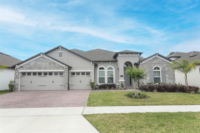 view of front of home with a front yard, stone siding, decorative driveway, and stucco siding