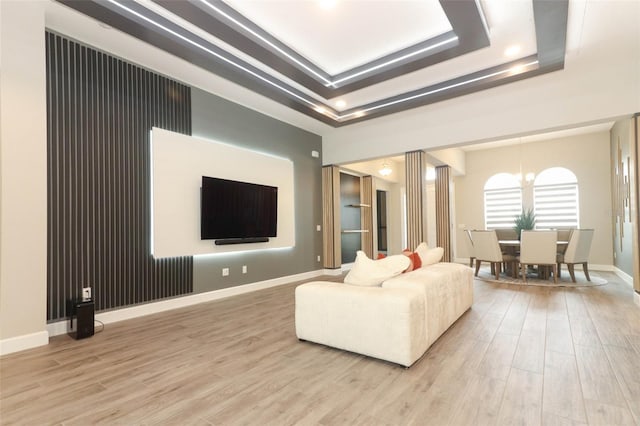 living area with a tray ceiling, wood finished floors, baseboards, and a notable chandelier