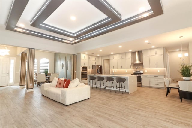 living room with light wood-type flooring, a raised ceiling, and a chandelier
