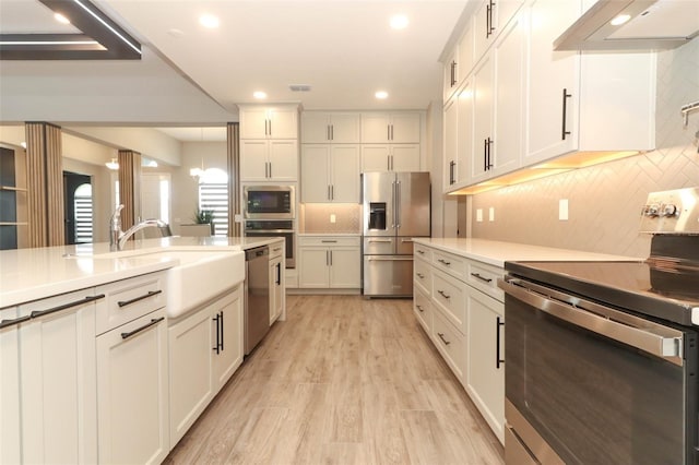 kitchen with light wood-style floors, appliances with stainless steel finishes, light countertops, a sink, and extractor fan