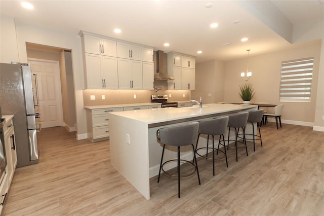 kitchen featuring a kitchen breakfast bar, tasteful backsplash, light wood-type flooring, wall chimney range hood, and appliances with stainless steel finishes
