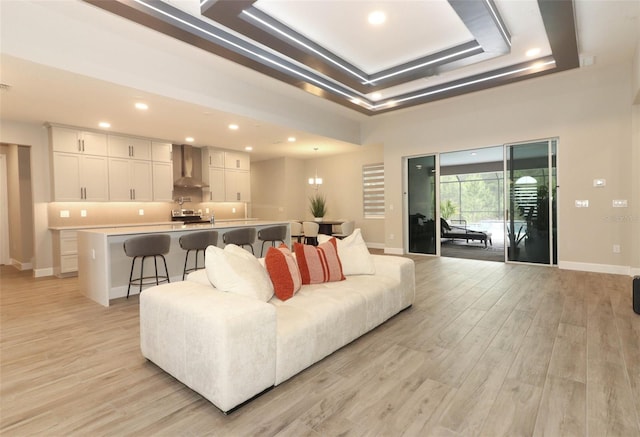 living room featuring a tray ceiling, light wood-type flooring, baseboards, and recessed lighting