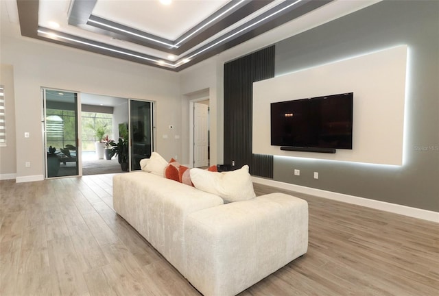 living area with a tray ceiling, baseboards, and light wood finished floors