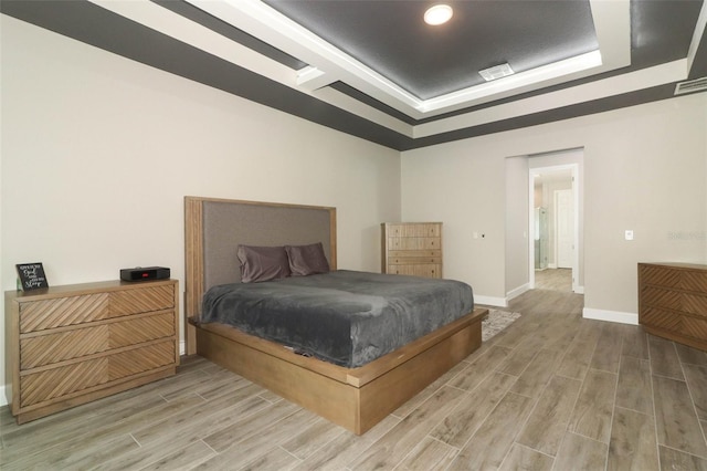 bedroom with a raised ceiling, visible vents, baseboards, and wood tiled floor