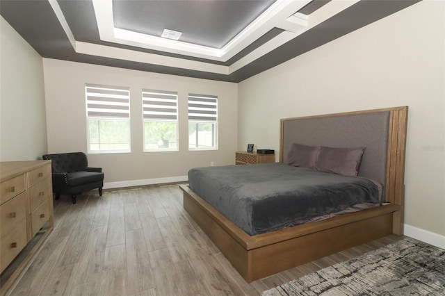 bedroom featuring visible vents, baseboards, a raised ceiling, and wood finished floors