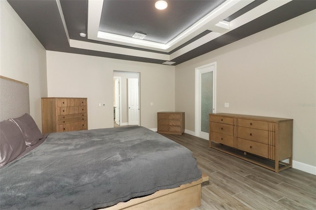 bedroom with a tray ceiling, baseboards, and wood finished floors