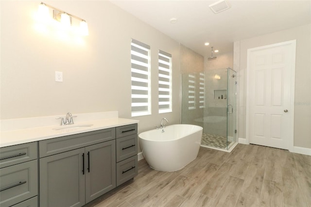 full bath with baseboards, a freestanding tub, a shower stall, vanity, and wood finished floors