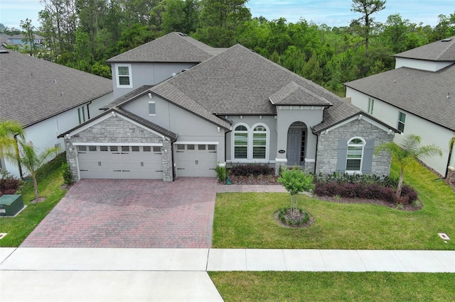 view of front of home with decorative driveway, a front yard, stone siding, an attached garage, and a shingled roof