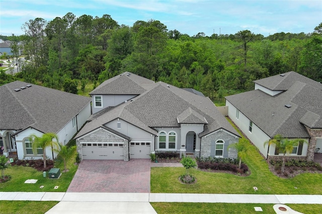 exterior space featuring an attached garage, stone siding, stucco siding, a front lawn, and decorative driveway