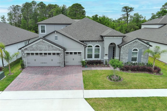 view of front of home featuring a front yard, stone siding, a garage, stucco siding, and decorative driveway
