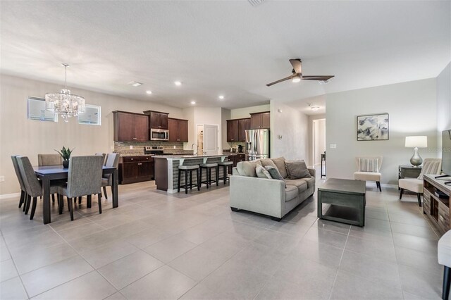 living area featuring light tile patterned floors, baseboards, recessed lighting, and ceiling fan with notable chandelier