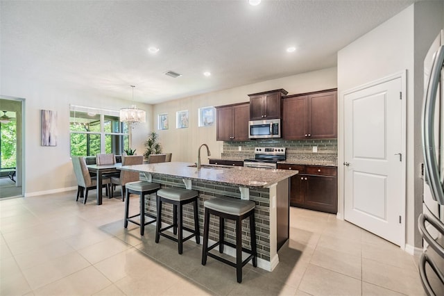 kitchen with visible vents, appliances with stainless steel finishes, a kitchen breakfast bar, a kitchen island with sink, and decorative backsplash