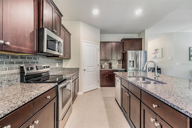 kitchen featuring light tile patterned floors, a sink, dark brown cabinets, stainless steel appliances, and light stone counters