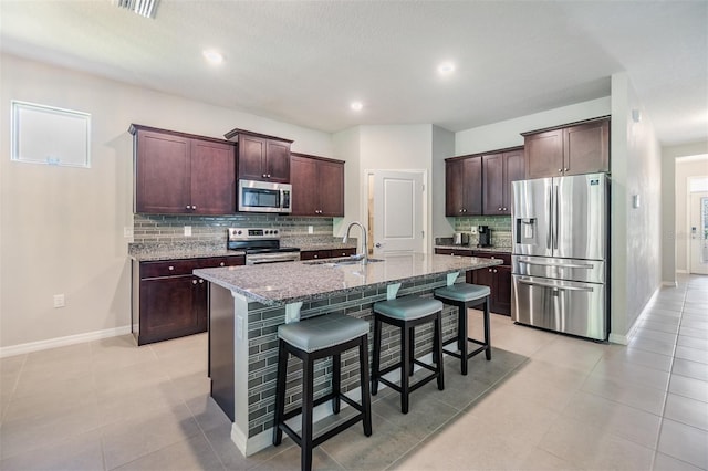 kitchen featuring a sink, appliances with stainless steel finishes, a kitchen breakfast bar, a kitchen island with sink, and light stone counters